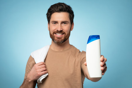 Happy middle aged bearded man showing blank shampoo bottle to camera and smiling, standing over blue background, mockupの写真素材