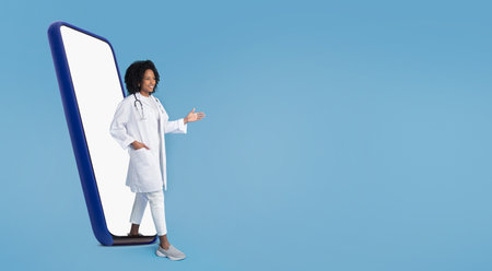 Happy confident millennial black lady in white coat with stethoscope,greeting on big phone screenの写真素材