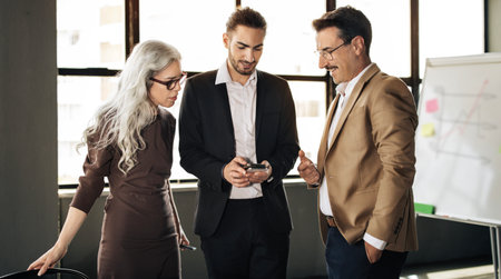 Three Successful Colleagues Using Business App On Smartphone In Office