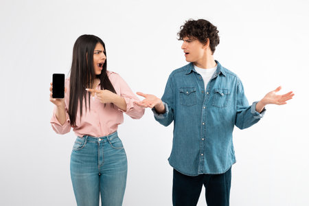 Angry Girlfriend Showing Phone Screen To Confused Boyfriend, White Background