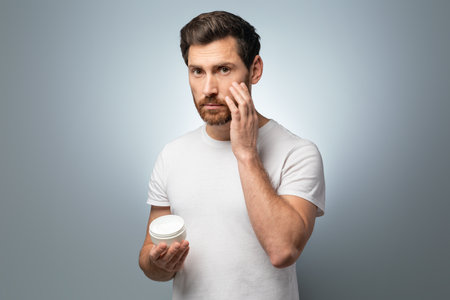Grooming essentials. Middle aged man applying moisturising cream on face while standing on grey studio backgroundの写真素材