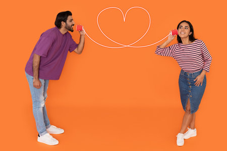Young indian couple with can phone on orange backgroundの写真素材
