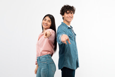 Smiling Young Couple Pointing Fingers Towards Camera On White Backgroundの写真素材
