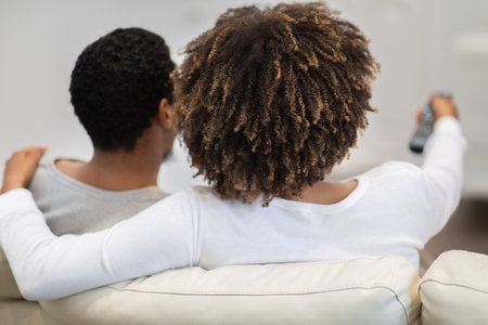 Rear view of black couple watching TV at homeの写真素材