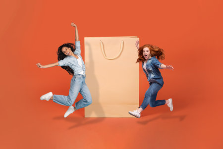 Happy young ladies jumping next to huge shopping bagの写真素材