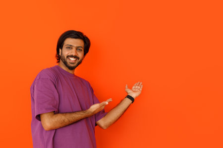 Happy indian guy in purple pointing at copy space, orangeの写真素材
