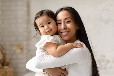 Asian Mommy Tenderly Hugging Her Little Child Girl In Bedroomの写真素材