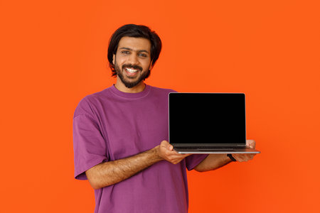 Positive indian man showing laptop with blank screen on orangeの写真素材