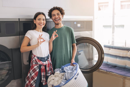 Couple Gesturing OK Posing Near Laundromat Washing Machines At Laundryの写真素材