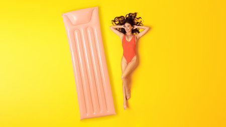 Woman In Swimsuit Lying Near Inflatable Mattress Over Yellow Backgroundの写真素材