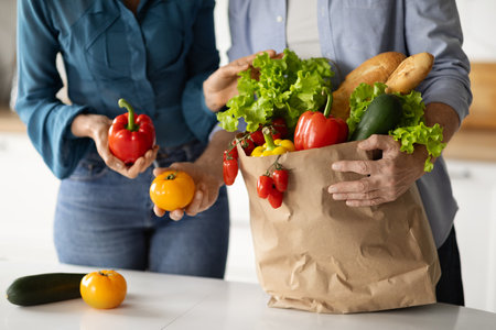 Unrecognizable Mature Couple Unpacking Paper Bag With Fresh Organic Vegetables In Kitchenの写真素材