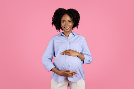Happy young pregnant african american curly woman in casual touching big belly, enjoy future motherhoodの写真素材