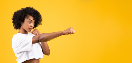 Serious confident millennial african american curly woman in white t-shirt fighting, punchingの写真素材