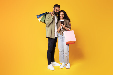 Middle Eastern Spouses Using Mobile Phone Shopping On Yellow Backgroundの写真素材