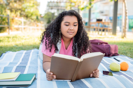 Hispanic Student Woman Learning Reading Book Outdoors Lying On Blanketの写真素材