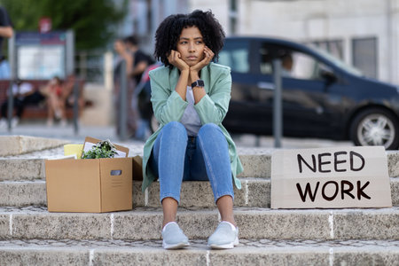 Upset unemployed young black woman sitting by need work signの写真素材