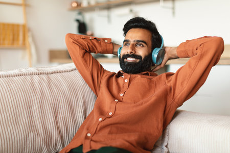 Cheerful indian man listening to music in headset at homeの写真素材