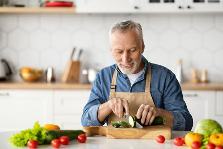 Portrait of smiling senior man cooking vegetable meal in kitchenの写真素材