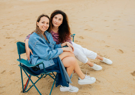 Cheerful millennial european women students in casual sit on chairs, enjoy free time on beach at weekendの写真素材