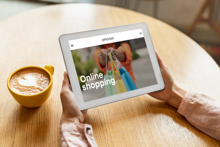 Young woman with coffee cup sitting in cafe, using tablet with fashion store on screen, enjoying online shoppingの写真素材
