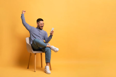 Great News. Joyful Asian Man Looking At Smartphone Screen And Celebrating Successの写真素材