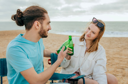 Smiling millennial european lady and arab guy in casual cheers bottles of beer, enjoy weekend on beachの写真素材