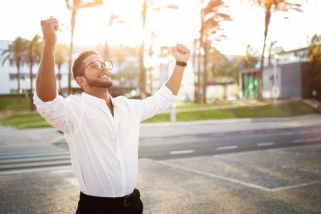 Overjoyed european businessman celebrating victory with clenched fists, staying outdoors after successful meetingの写真素材