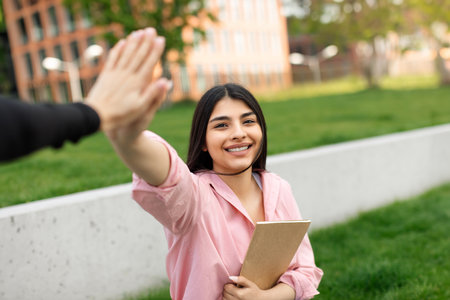 Happy hispanic lady giving high five, celebrating academic success and passed exam, walking in college campus outdoorsの写真素材