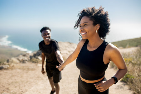 Happy black lady leading man by hand on rocks near ocean, enjoy break from morning workout outdoorsの写真素材