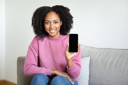 Glad millennial black woman show smartphone with empty screen, recommending app, websiteの写真素材