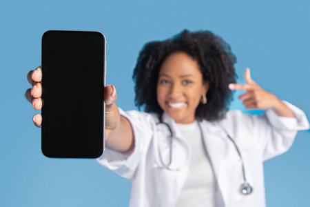 Happy excited young back curly lady doctor in coat point finger at phone, focus on blank screen