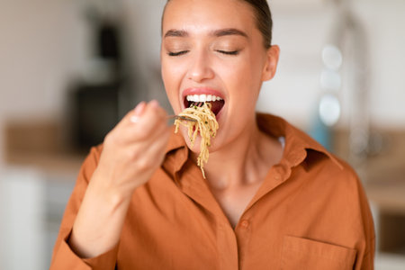 Home cooked delights. Woman eating delicious homemade pasta, enjoying tasty lunch, sitting at table in kitchen, closeupの写真素材
