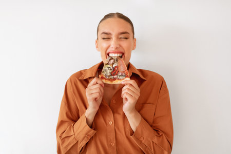 Excited woman enjoying pizza holding and biting tasty slice standing on white background. Unhealthy nutrition cheat mealの写真素材