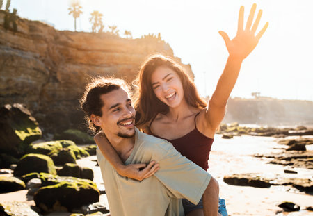 Positive millennial arabic man student hold caucasian woman on back, play game, have fun, enjoy summerの写真素材