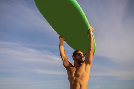 Young Muscular Male Surfer Holding Surfboard Over Head And Looking Asideの写真素材