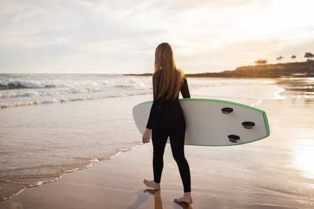 Solo Surfer. Young Woman In Wetsuit Carrying Surfboard Going Into Oceanの写真素材