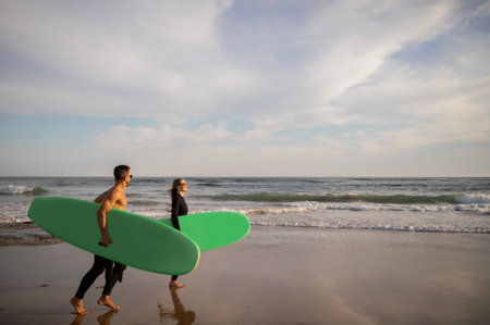 Summer Activities. Happy Young Couple Carrying Surfboards Walking Along Shorelineの写真素材