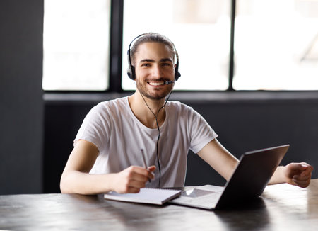 Middle Eastern Guy Using Laptop Posing With Headset In Office