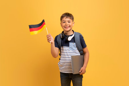 Cheerful school boy showing flag of Germany, yellow background