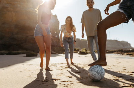 Happy millennial diverse people students playing soccer ball, enjoy summer vacation, have fun on beachの写真素材