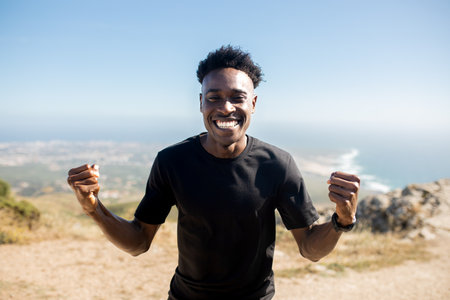 Overjoyed african american man in sportswear celebrating victory and great workout result, great view on ocean, outdoorの写真素材