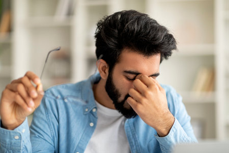 Exhausted Young Indian Man Taking Off Glasses, Feeling Eyes Fatigue After Work