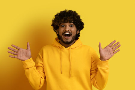 Amazed young eastern guy gesturing and grimacing on yellowの写真素材