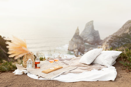 Beautiful romantic picnic with wine bottle and glasses, blanket, pillows and decor on rocks, breathtaking view on ocean shoreの写真素材