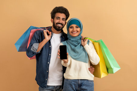 Online Shopping App. Cheerful young muslim couple showing smartphone with blank screenの写真素材