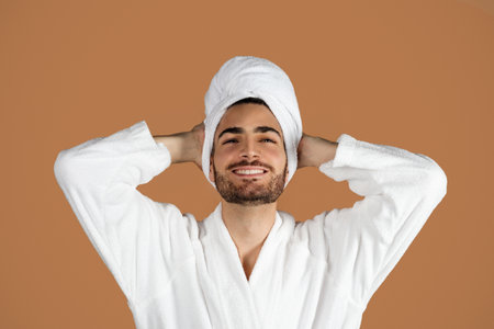 Arabic Young Man Posing In White Bathrobe On Brown Backgroundの写真素材