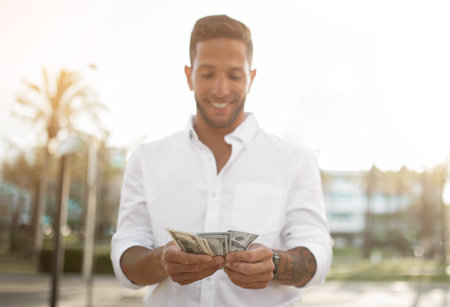 First salary. Happy young businessman holding fan of money, celebrating financial luck and success, standing outdoorsの写真素材