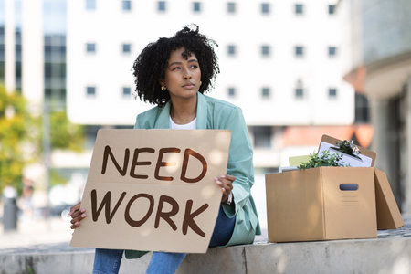 Unhappy young african american lady sitting on street, need workの写真素材