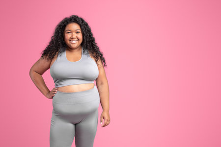 Happy black plus size woman athlete in sportswear smiling at camera, posing on pink background, studio, free spaceの写真素材