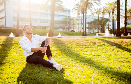 Work life balance concept. Happy young european businessman sitting on grass in park, having break and resting, free spaceの写真素材